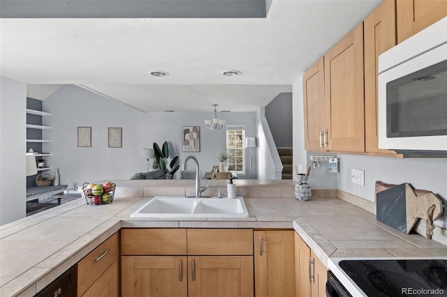 kitchen with tile countertops, a chandelier, white microwave, a sink, and open floor plan