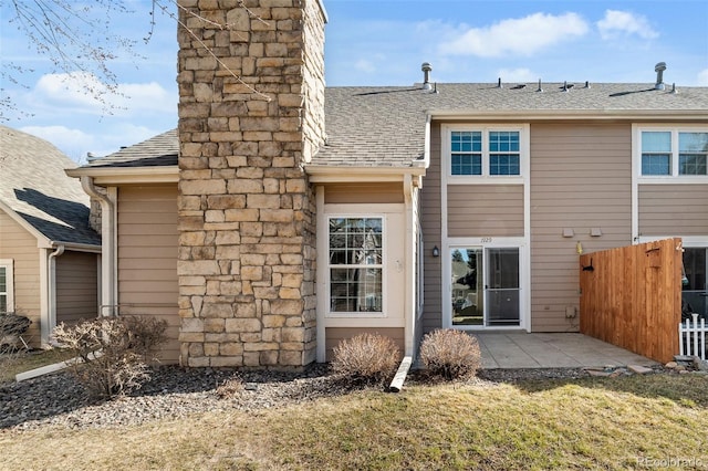 back of property featuring a patio area, a chimney, fence, and roof with shingles