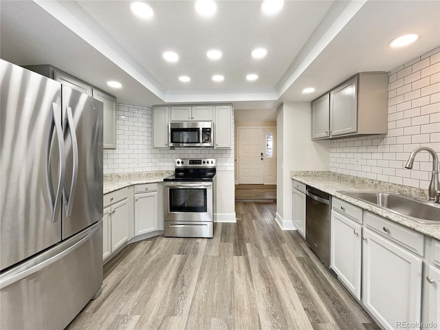 kitchen featuring tasteful backsplash, stainless steel appliances, light wood-type flooring, sink, and a tray ceiling