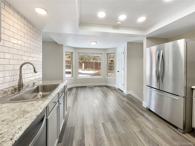 kitchen featuring appliances with stainless steel finishes, backsplash, light wood-type flooring, and sink