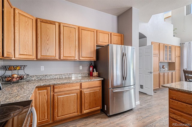 kitchen featuring wood-type flooring, stove, stainless steel fridge, and light stone counters