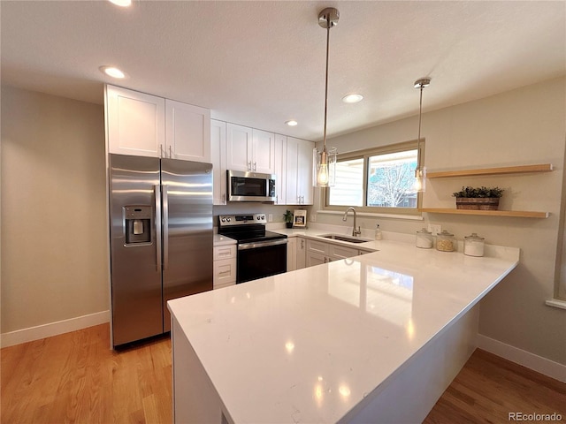 kitchen with white cabinetry, sink, kitchen peninsula, decorative light fixtures, and appliances with stainless steel finishes