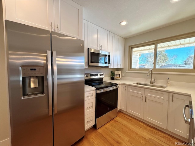 kitchen with white cabinets, appliances with stainless steel finishes, light wood-type flooring, and sink