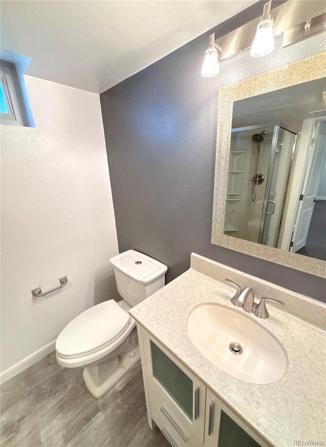 bathroom featuring toilet, vanity, a shower with shower door, and hardwood / wood-style flooring