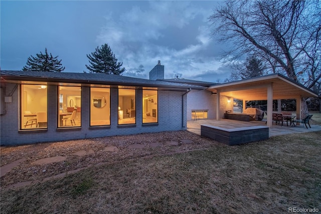 back of property with brick siding, a patio area, a chimney, and a lawn