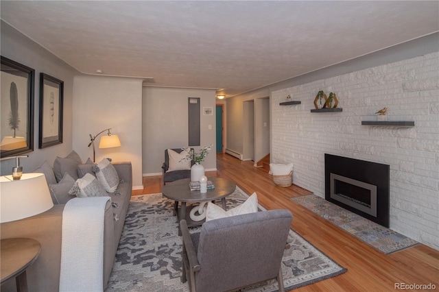 living room with a baseboard heating unit, baseboards, wood finished floors, and a fireplace