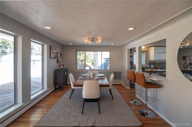 dining area with a textured ceiling, wood finished floors, visible vents, and a baseboard radiator