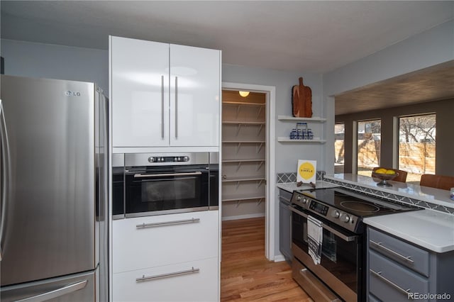 kitchen with light wood finished floors, gray cabinets, open shelves, appliances with stainless steel finishes, and light countertops