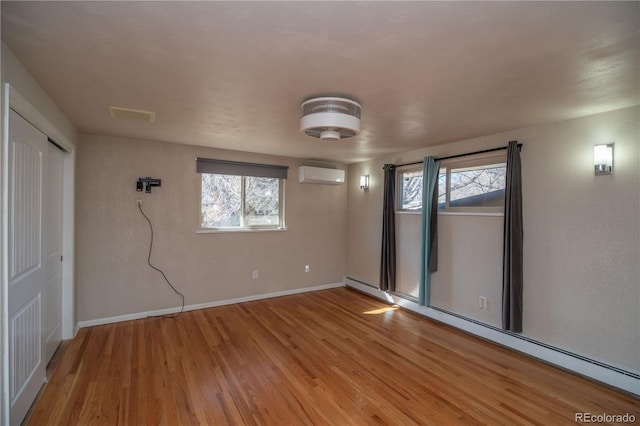 empty room with a wall mounted AC, a healthy amount of sunlight, wood finished floors, and a baseboard radiator