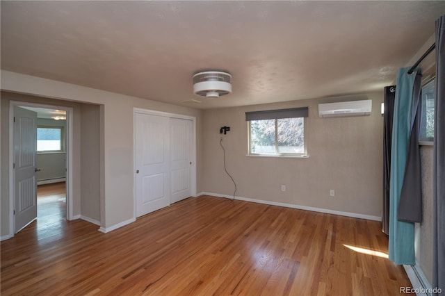 unfurnished bedroom with baseboards, baseboard heating, wood finished floors, and a wall unit AC