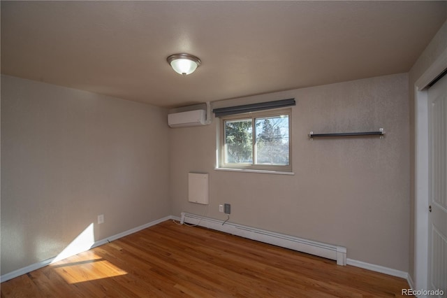 spare room with baseboard heating, a wall mounted AC, baseboards, and wood finished floors