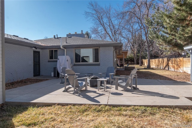 rear view of house with a patio, brick siding, an outdoor fire pit, and fence