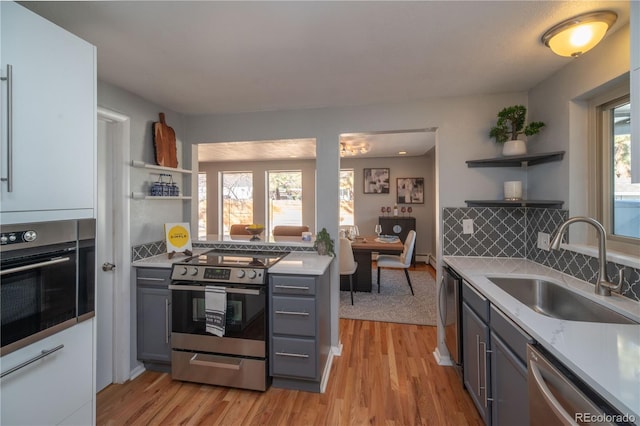 kitchen with open shelves, gray cabinetry, appliances with stainless steel finishes, and a sink