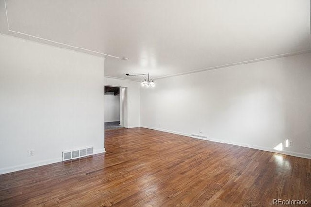 spare room featuring a chandelier, dark wood-type flooring, and ornamental molding