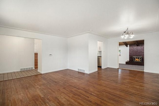 unfurnished living room featuring dark hardwood / wood-style flooring, an inviting chandelier, a brick fireplace, and crown molding