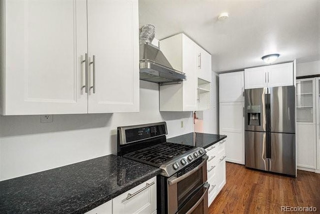 kitchen with wall chimney exhaust hood, dark hardwood / wood-style flooring, dark stone countertops, white cabinets, and appliances with stainless steel finishes