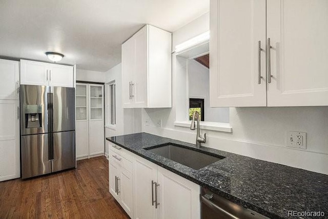 kitchen featuring stainless steel appliances, dark wood-type flooring, sink, dark stone countertops, and white cabinets