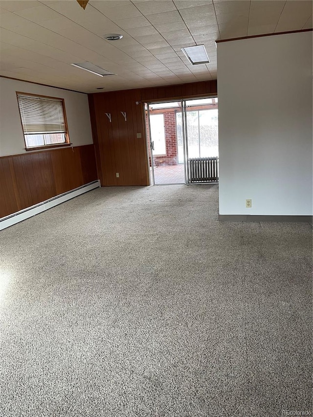 unfurnished room featuring baseboard heating, wooden walls, and radiator