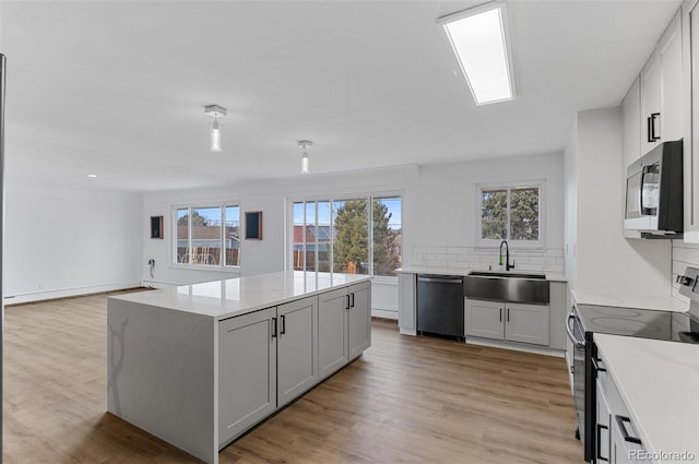 4731 W 66th Ave, Arvada, CO 80003 - kitchen featuring appliances with stainless steel finishes, a sink, a kitchen island, tasteful backsplash, and light wood finished floors