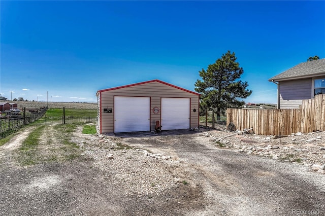 detached garage with a rural view and fence