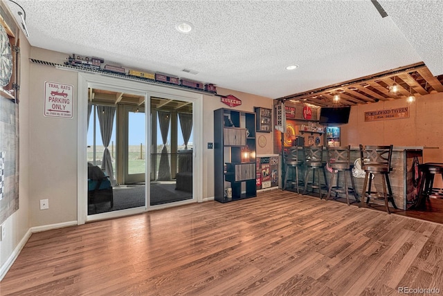 interior space with baseboards, a textured ceiling, a bar, visible vents, and wood finished floors