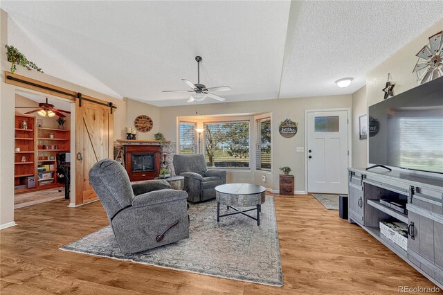 living area with baseboards, a barn door, a ceiling fan, light wood-style floors, and a textured ceiling