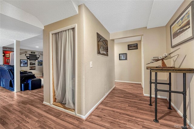 hall featuring baseboards, wood finished floors, and a textured ceiling