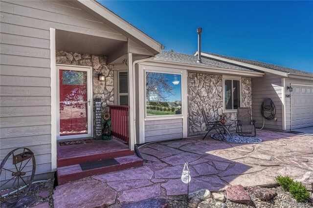 view of exterior entry with stone siding, a garage, and roof with shingles