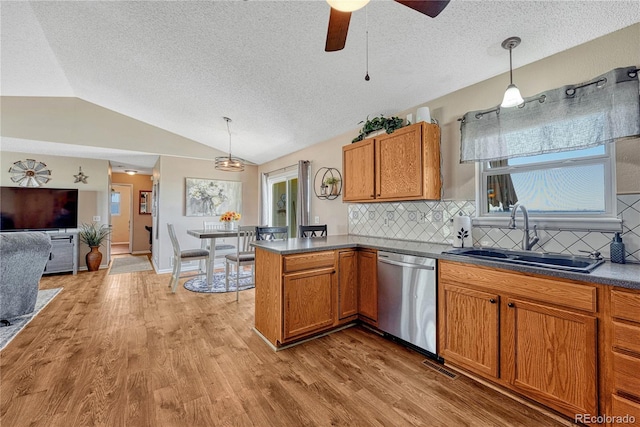 kitchen with dishwasher, a sink, a textured ceiling, brown cabinetry, and vaulted ceiling