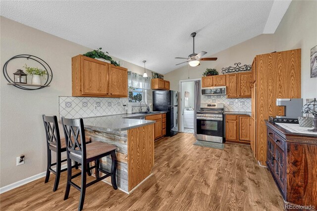 kitchen with vaulted ceiling, a peninsula, brown cabinetry, stainless steel appliances, and a sink