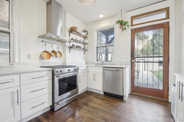 kitchen featuring appliances with stainless steel finishes, range hood, a sink, white cabinets, and light stone counters