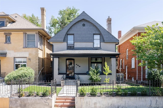 view of front facade with a porch, a fenced front yard, brick siding, and a chimney