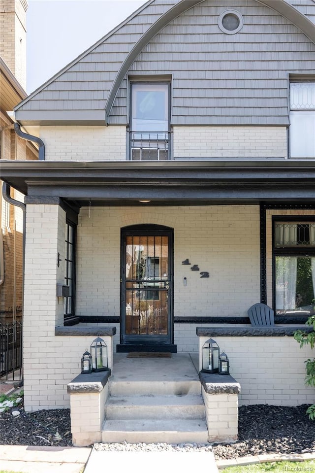 entrance to property with brick siding, a porch, and a balcony