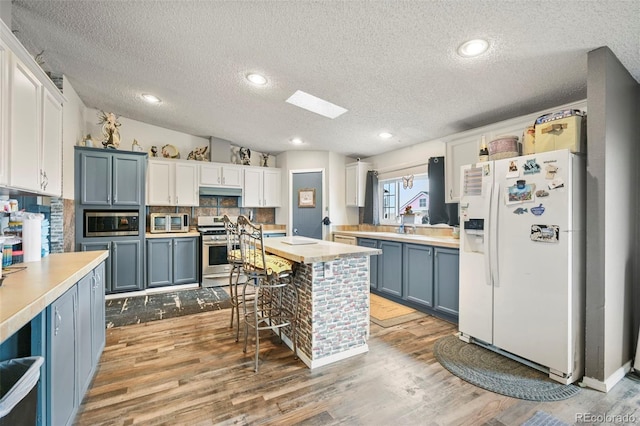 kitchen featuring a textured ceiling, white cabinets, stainless steel appliances, and light wood-type flooring