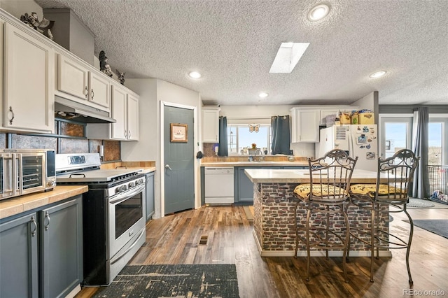 kitchen featuring white cabinets, a textured ceiling, dark hardwood / wood-style floors, a skylight, and white appliances