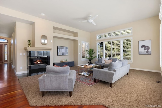living area featuring a ceiling fan, a tile fireplace, wood finished floors, and baseboards