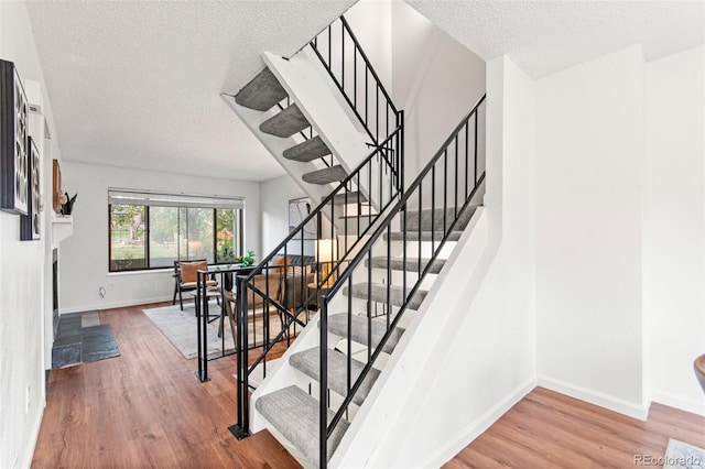 stairway with a textured ceiling, wood finished floors, and baseboards