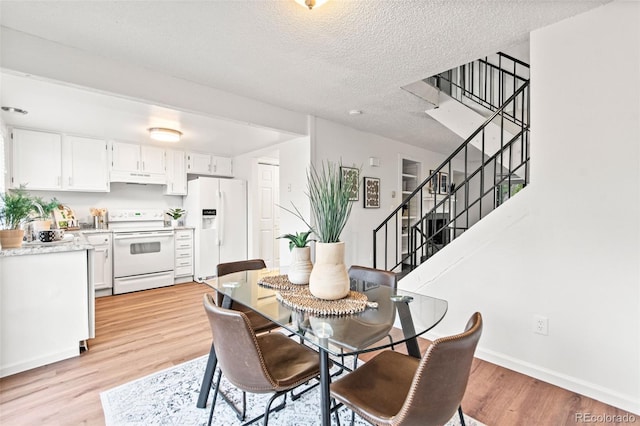 dining area with stairway, light wood-type flooring, a textured ceiling, and baseboards