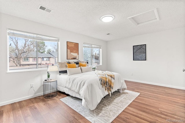 bedroom with attic access, multiple windows, wood finished floors, a textured ceiling, and baseboards