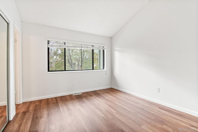 unfurnished bedroom with wood finished floors, vaulted ceiling, a textured ceiling, and baseboards