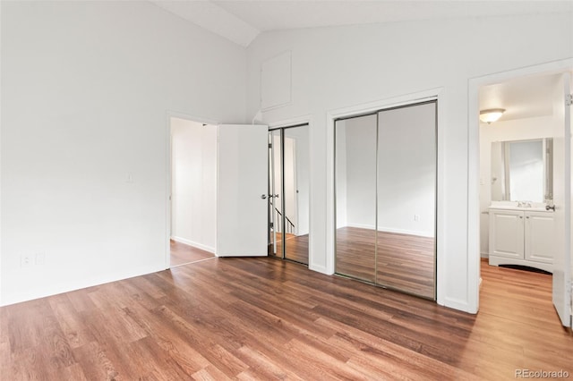 unfurnished bedroom featuring multiple closets, wood finished floors, high vaulted ceiling, and a sink