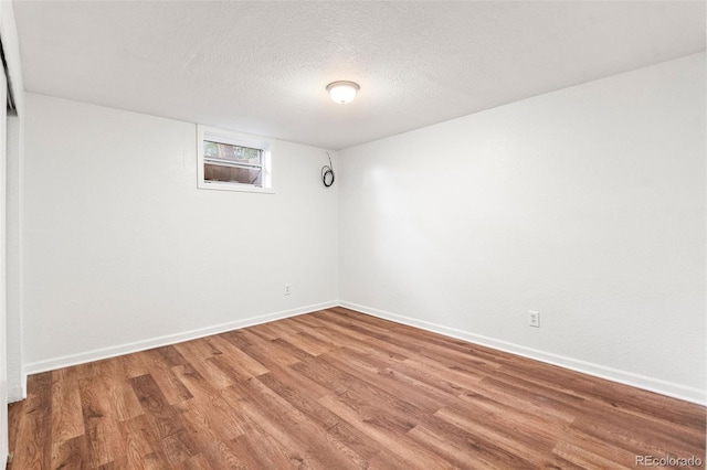 empty room featuring light wood finished floors, baseboards, and a textured ceiling