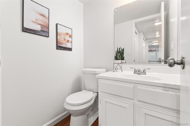 half bathroom with vanity, toilet, wood finished floors, and baseboards