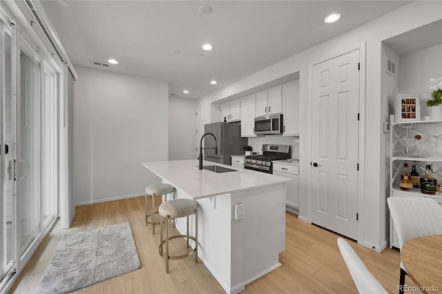4612 S Wenatchee St Unit A, Aurora, CO 80015 - kitchen with appliances with stainless steel finishes, a kitchen island with sink, white cabinetry, light wood-type flooring, and recessed lighting