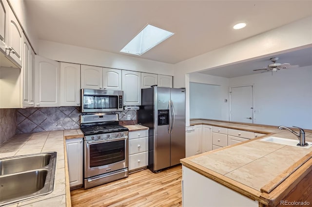 kitchen featuring light wood-style flooring, stainless steel appliances, a skylight, and a sink