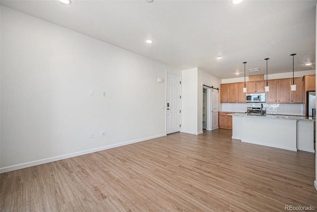 kitchen with open floor plan, stainless steel appliances, a barn door, and light wood-type flooring