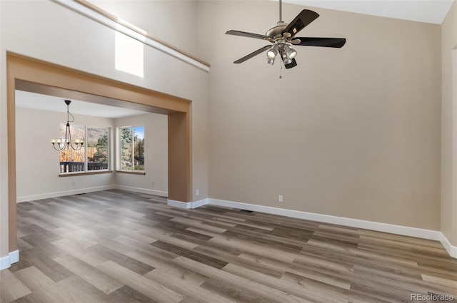 unfurnished room with ceiling fan with notable chandelier, baseboards, and wood finished floors