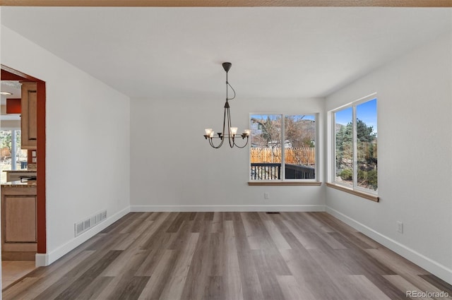 unfurnished dining area with visible vents, a notable chandelier, baseboards, and wood finished floors