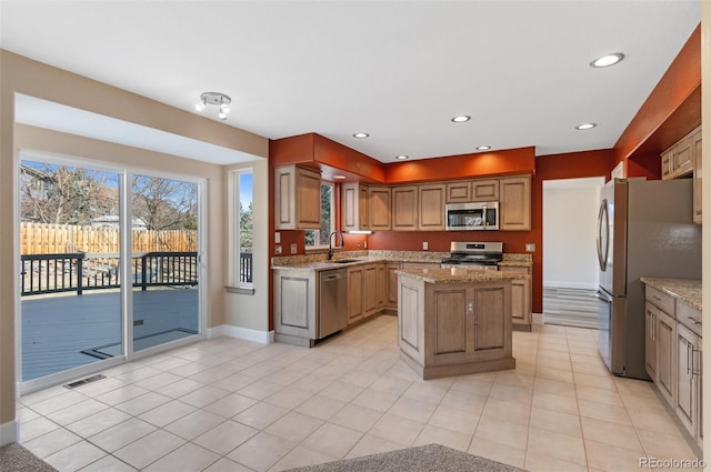 kitchen featuring visible vents, a kitchen island, light stone counters, stainless steel appliances, and a sink