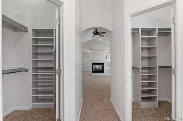 spacious closet with arched walkways, carpet flooring, vaulted ceiling, ceiling fan, and a multi sided fireplace